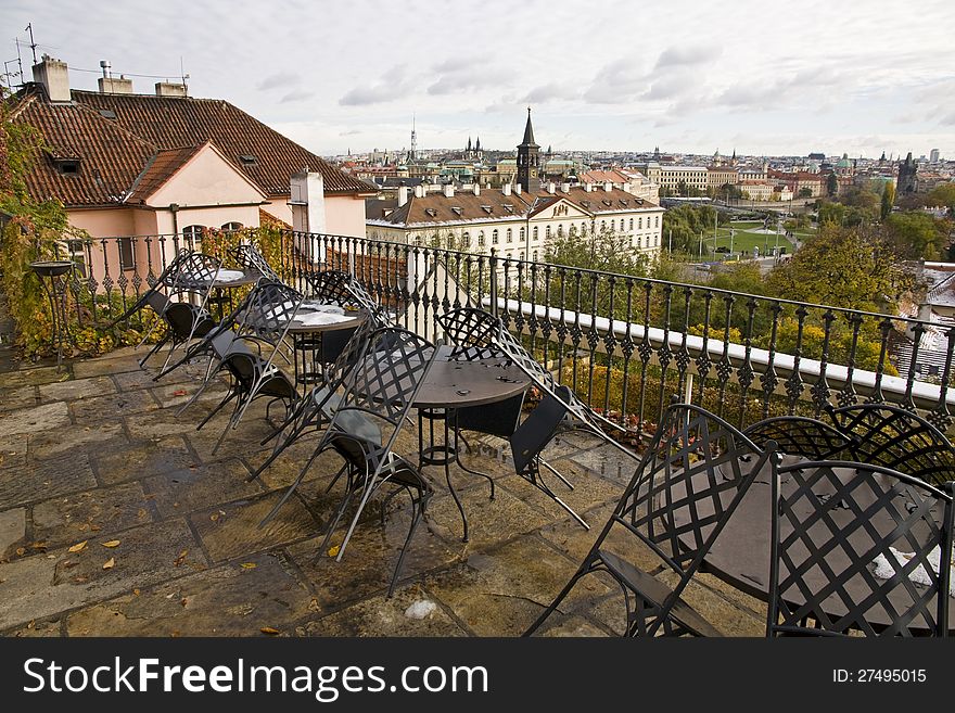 Outdoor seating with black tables and chairs in a restaurant near the prague castle in the czech republic, in the background are the roofs of the old town. Outdoor seating with black tables and chairs in a restaurant near the prague castle in the czech republic, in the background are the roofs of the old town