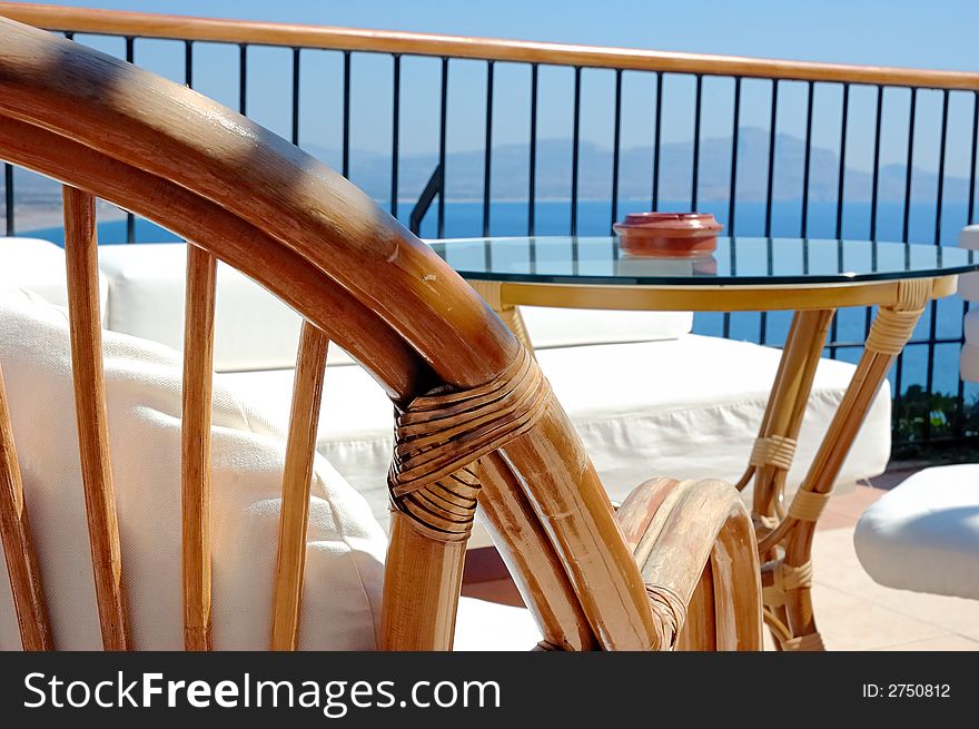 Back of chair and glass table in the bar of a luxury hotel, bright sun, see view in background. Back of chair and glass table in the bar of a luxury hotel, bright sun, see view in background