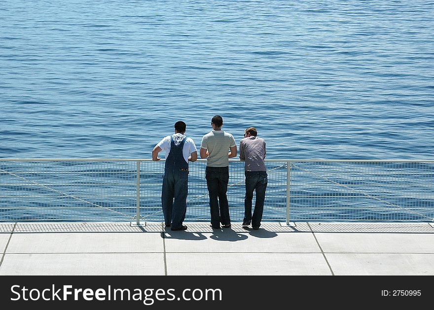 Friends standing on a bridge looking at the calm waters.