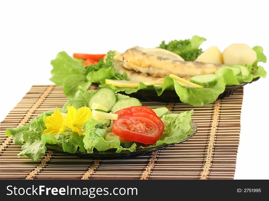 A plate with salad, on a background a dish with fried fish. A plate with salad, on a background a dish with fried fish.