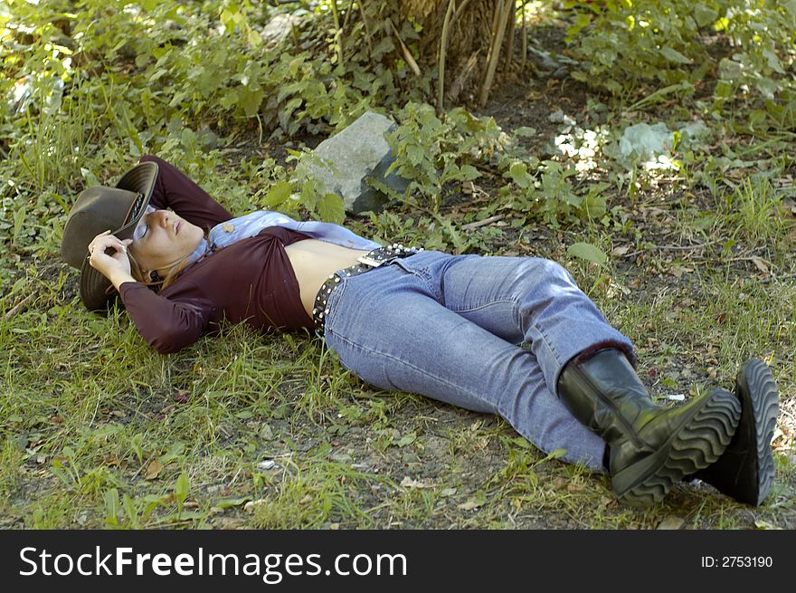 A smiling woman wearing a cowboy hat and lying down in the grass. A smiling woman wearing a cowboy hat and lying down in the grass