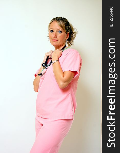 A nurse in pink scrubs holds on to her stethescope. A nurse in pink scrubs holds on to her stethescope.