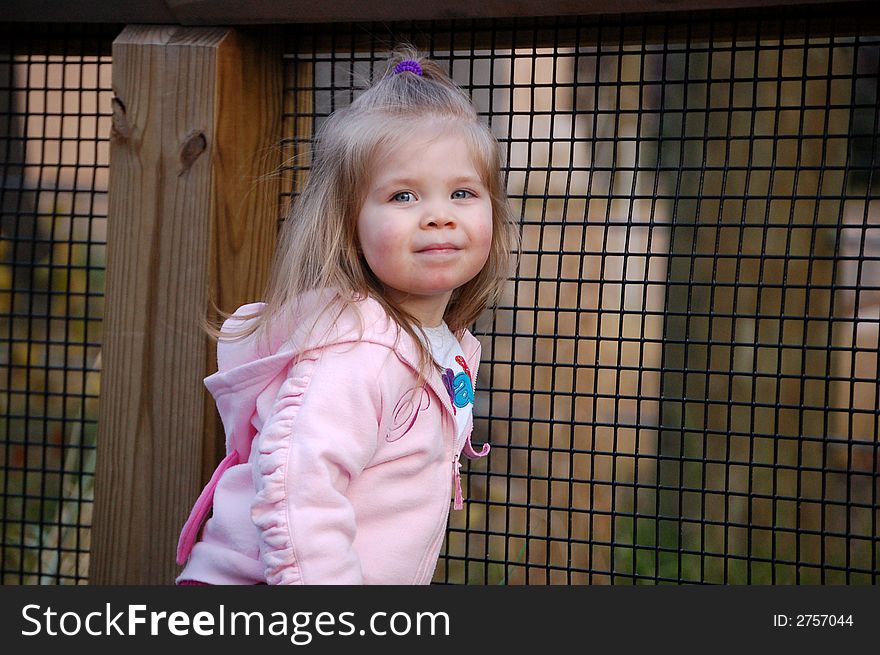 Two year old girl peeking through a fence. Two year old girl peeking through a fence.