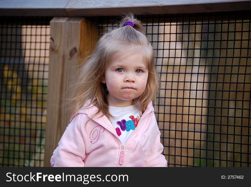 Two year old girl in pink looking bashful or shy.