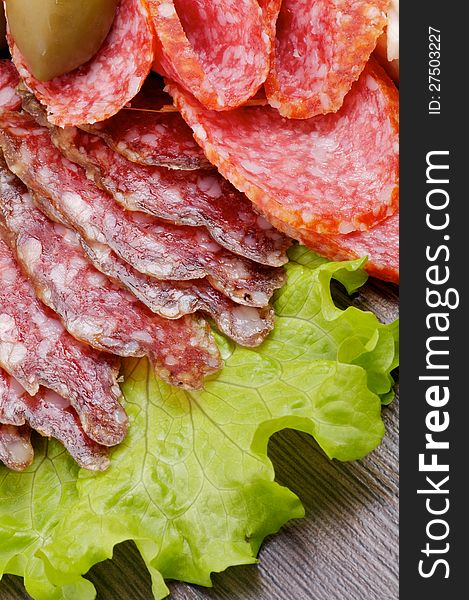 Slices of Salami and Smoked Sausage on Lettuce with Green Olive closeup