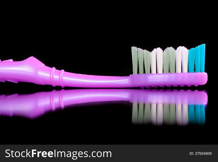 A bright pink toothbrush with multicolored bristles and reflection on a black background. A bright pink toothbrush with multicolored bristles and reflection on a black background