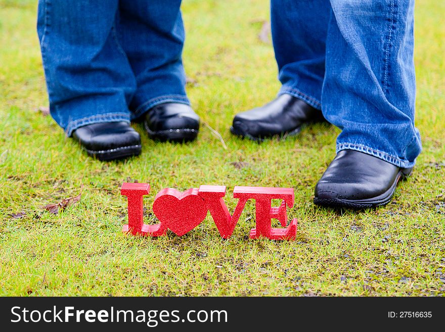 The feet of a couple with the word love in red on the green grass. The feet of a couple with the word love in red on the green grass.