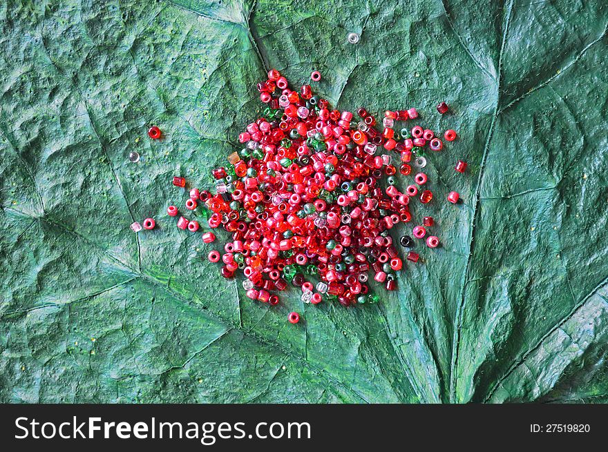 The pile of red, pink and green beads on the green leaf. The pile of red, pink and green beads on the green leaf