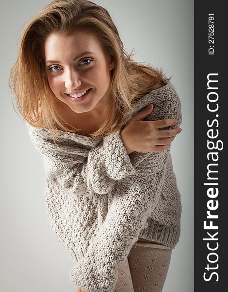 Beautiful blond young woman in knitted jumper and stockings stands on gray background. Beautiful blond young woman in knitted jumper and stockings stands on gray background