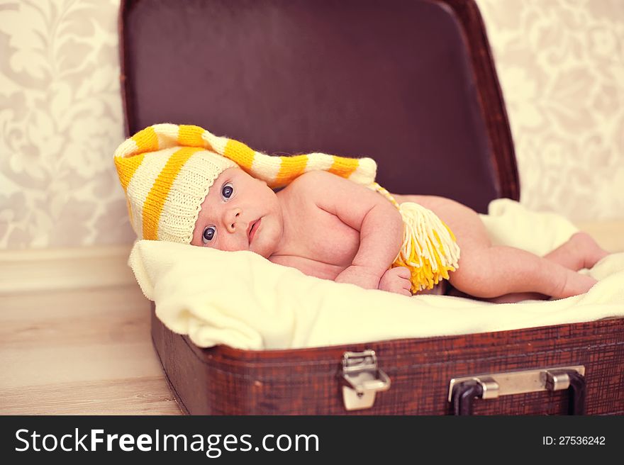 Naked baby in a warm hat is in the suitcase. Naked baby in a warm hat is in the suitcase