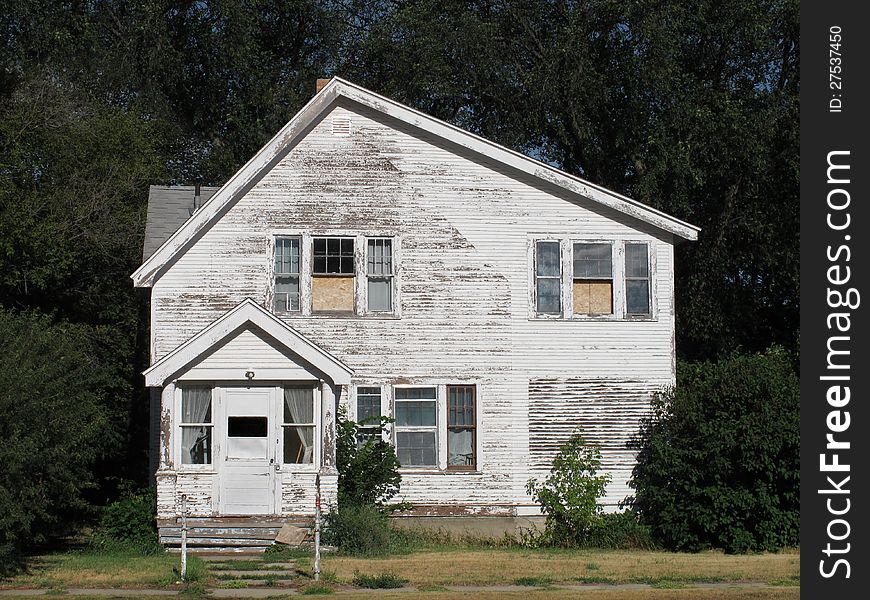 Old abandoned white wooden American house, surrounded by trees, grass, and weeds. Old abandoned white wooden American house, surrounded by trees, grass, and weeds.