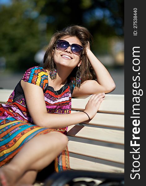 Attractive girl sitting on wooden bench in summer park