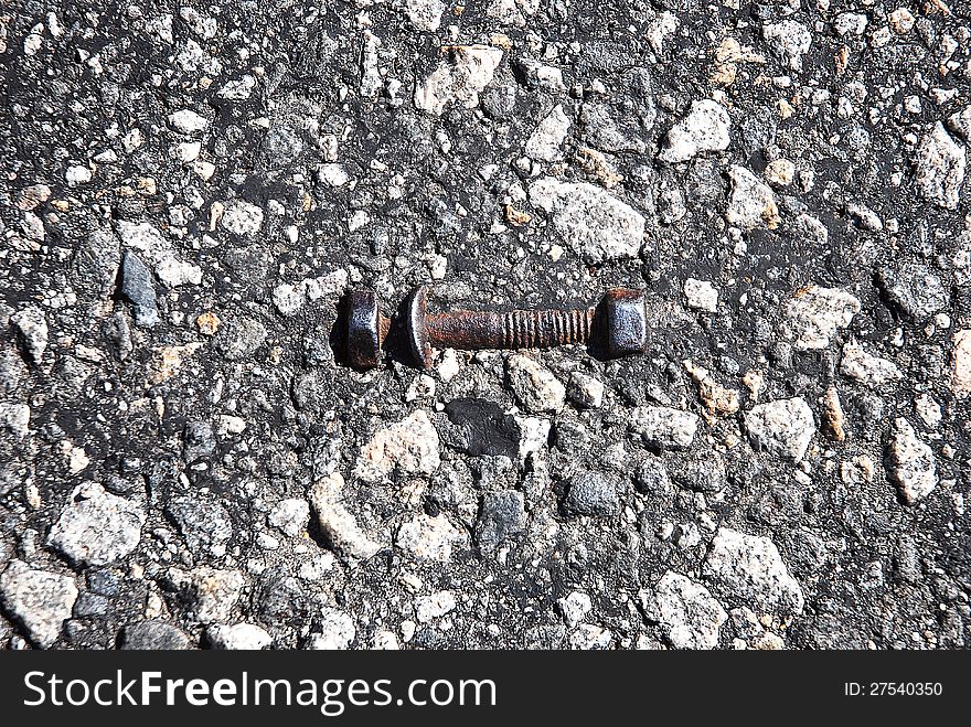 Rusty iron bolt and nut in the asphalt texture