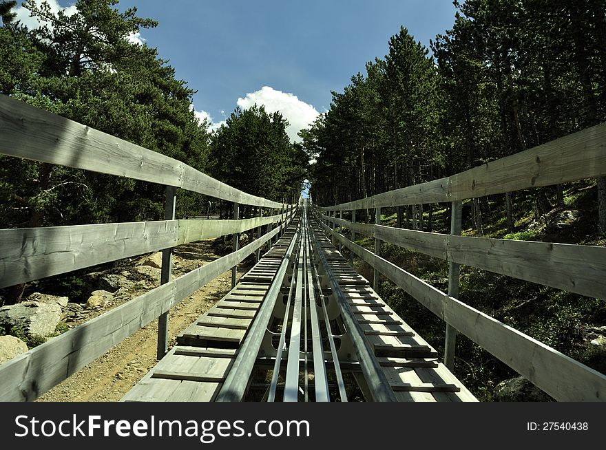 The track of an alpine roller coaster up to the peek, through the green forest in the summer. The track of an alpine roller coaster up to the peek, through the green forest in the summer