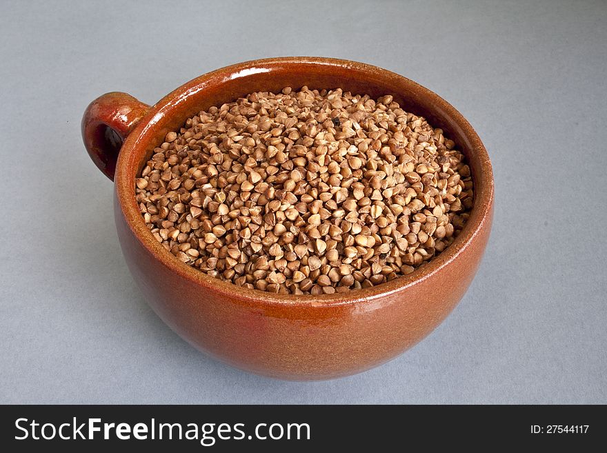 Dry buckwheat in ceramic bowl over gray background