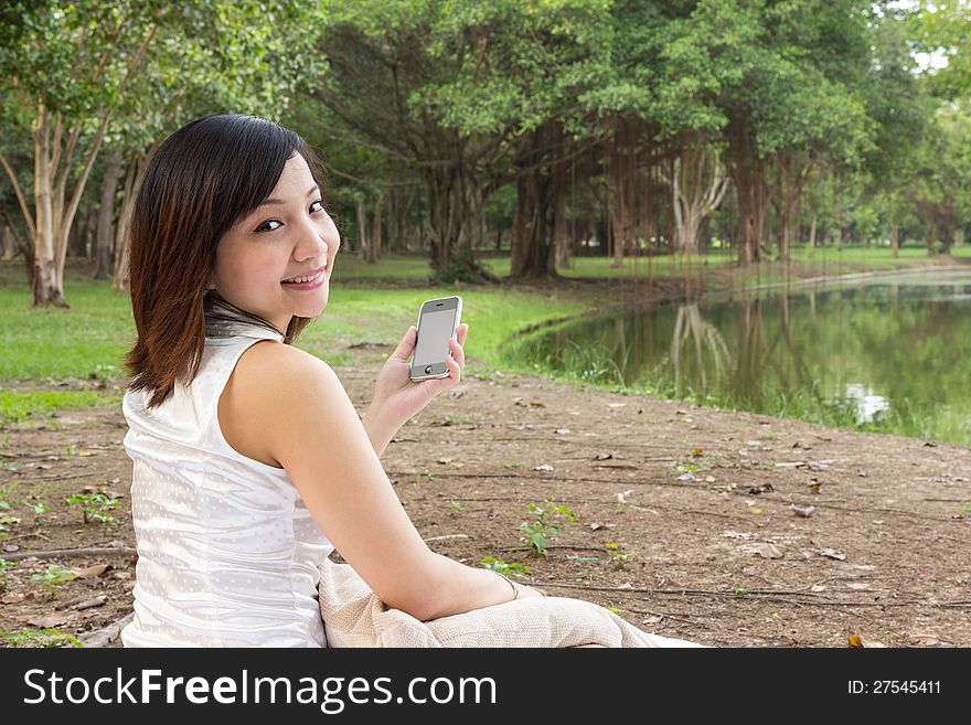 Asian woman with mobile phone and sitting at park