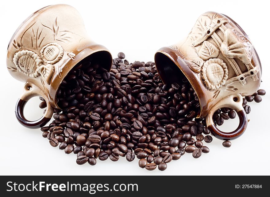 Hand made cups spill the coffee beans. Hand made coffee cups with spilt whole coffee beans closeup isolated on white.