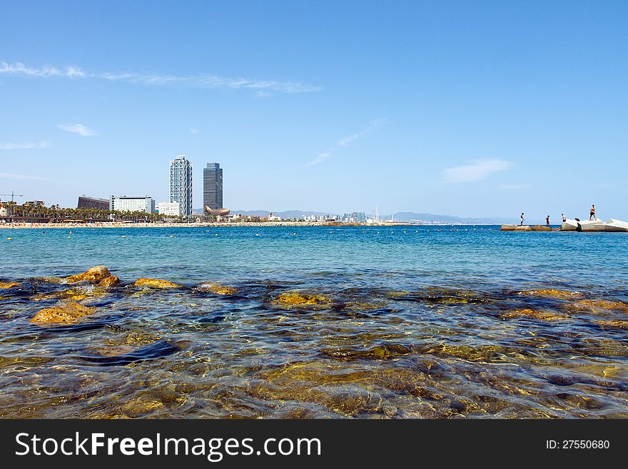 Wide angle view of a beach in Barcelona, Spain, with blue water, a clear sky and skyscrapers in the background. Wide angle view of a beach in Barcelona, Spain, with blue water, a clear sky and skyscrapers in the background