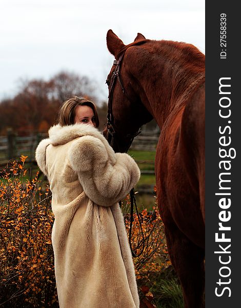 Pretty young woman in a fur coat stands holding her horse in Autumn. Pretty young woman in a fur coat stands holding her horse in Autumn.