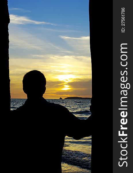 Silhouette of person standing between pillars and looking out to sea, an island, and a beautiful sunset. Silhouette of person standing between pillars and looking out to sea, an island, and a beautiful sunset.