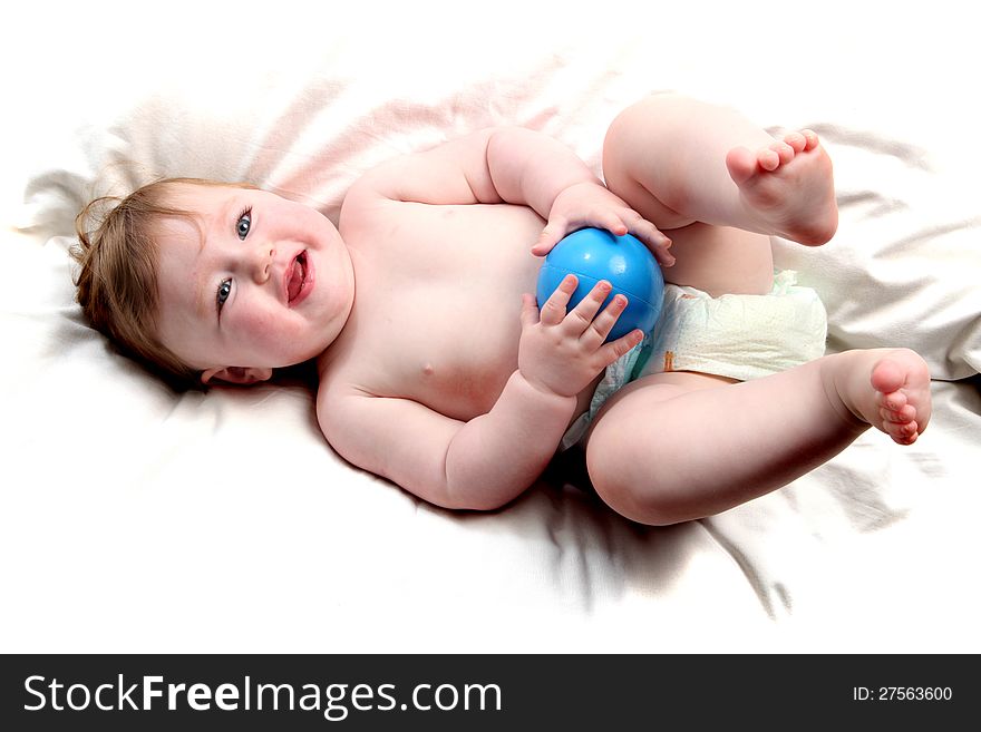 Baby girl lying on a white sheet playing with a blue ball. Baby girl lying on a white sheet playing with a blue ball