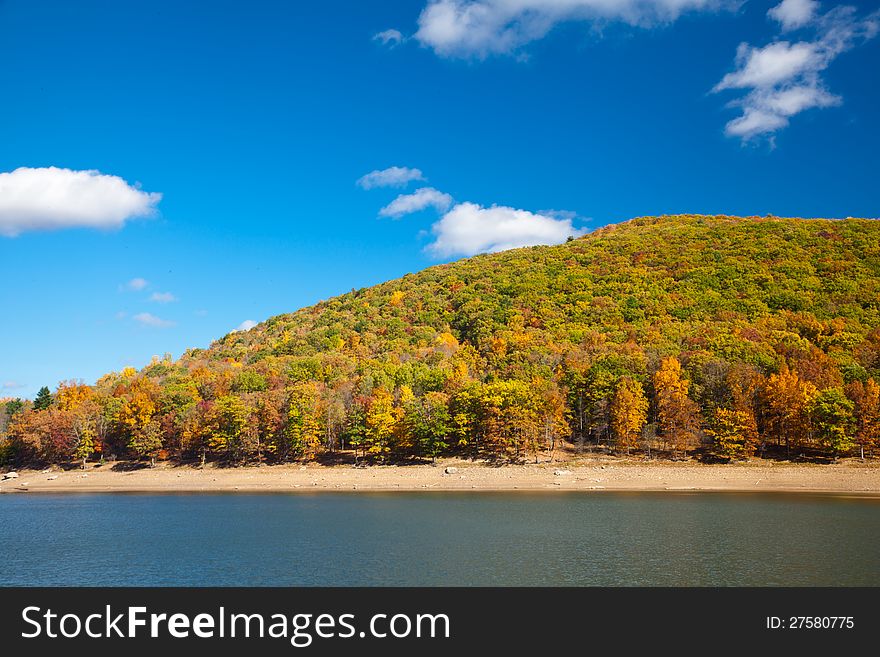 River surrounded by Autumn forest mountains under blue sky
