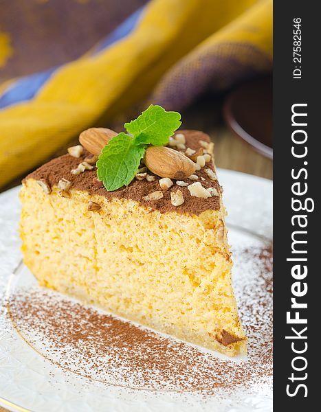 A piece of pumpkin cheesecake topped with cocoa and decorated with mint and almonds on a plate. A piece of pumpkin cheesecake topped with cocoa and decorated with mint and almonds on a plate