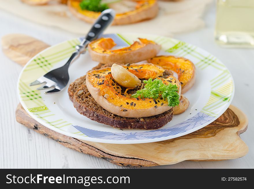 Appetizer - sliced ​​pumpkin baked with garlic and corn bread on a plate. Appetizer - sliced ​​pumpkin baked with garlic and corn bread on a plate