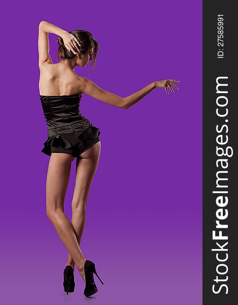Photo slender girl with excellent adorable legs on the high heels posing in the studio on purple background. Photo slender girl with excellent adorable legs on the high heels posing in the studio on purple background