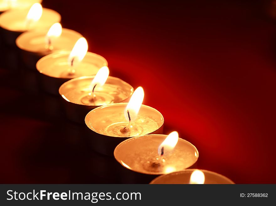 Set of lighting candles in a row on dark red background