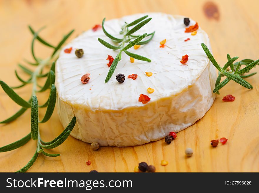 Whole form of brie cheese with rosemary and pepper over wooden background