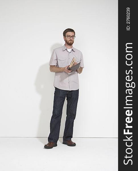 Man in a gray shirt and denim holding a brown book standing full length against a white studio wall. Man in a gray shirt and denim holding a brown book standing full length against a white studio wall.