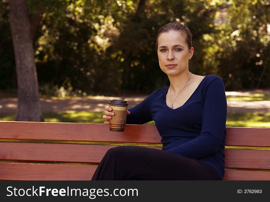 Woman sitting on a bench in a park during summer with a cup of coffee or tea in a cardboard cup. Woman sitting on a bench in a park during summer with a cup of coffee or tea in a cardboard cup.