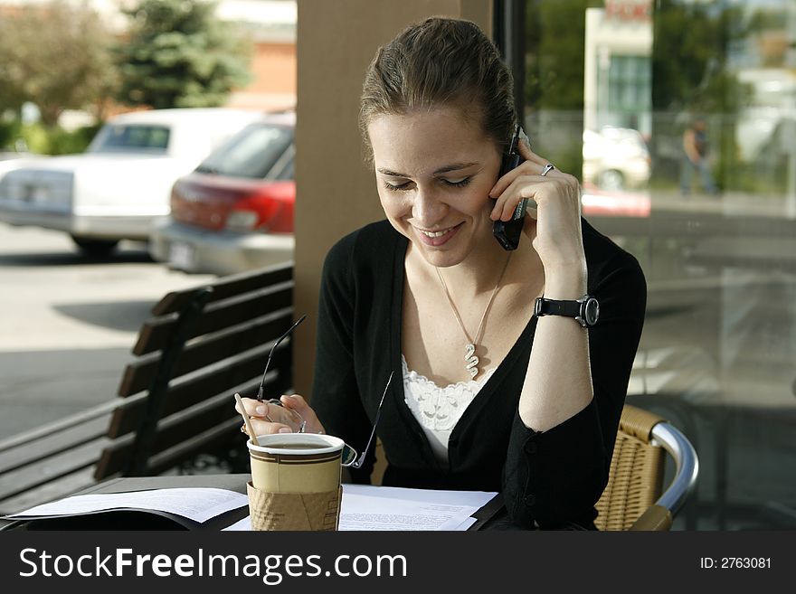 Young woman smiling while doing paperwork and talking on cell phone at cafe. Young woman smiling while doing paperwork and talking on cell phone at cafe.
