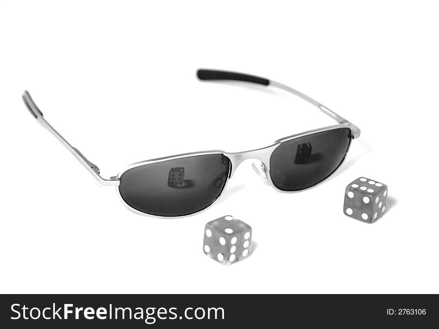 A pair of dice in front of sunglasses isolated  against a white background in black and white. . A pair of dice in front of sunglasses isolated  against a white background in black and white.