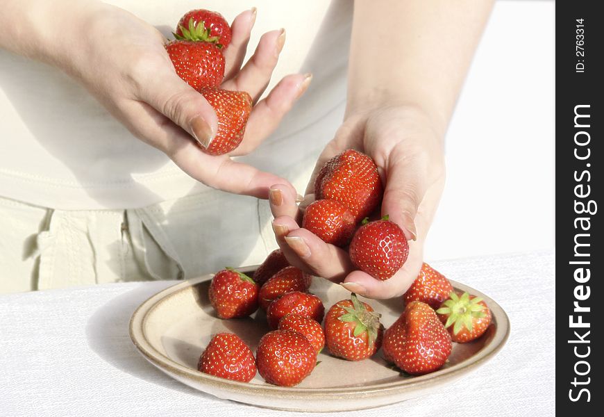 Hands of the girl a strawberry a ceramic plate a table a cloth white flax a background light. Hands of the girl a strawberry a ceramic plate a table a cloth white flax a background light