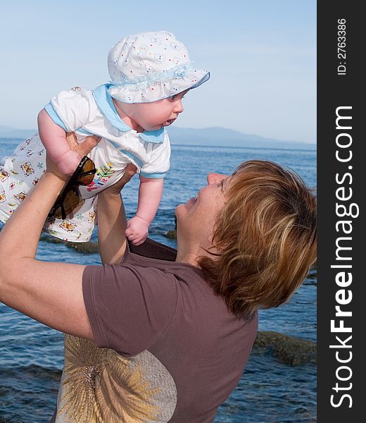 Family rest background representing mother holding her baby in the sky against sea landscape