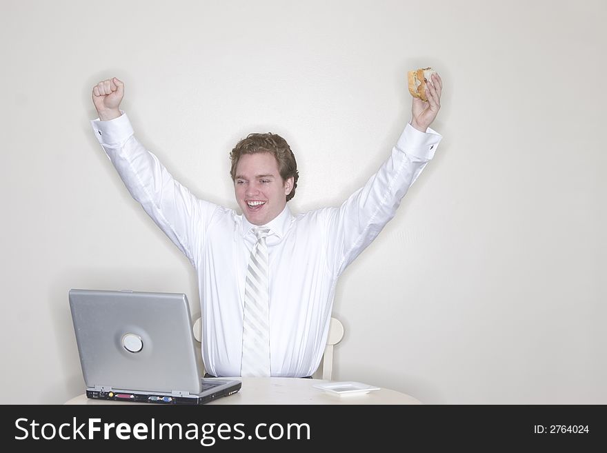 Businessman sitting at his table with his laptop and hands outstretched and in the air for success while holding his sandwich. Businessman sitting at his table with his laptop and hands outstretched and in the air for success while holding his sandwich