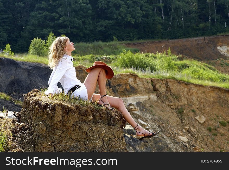 Woman wiht a cawboy hat sitting on an edge