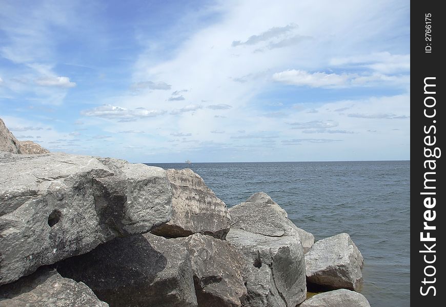 Huge rocks on the coast with water, and a cloudy blue sky. Huge rocks on the coast with water, and a cloudy blue sky.