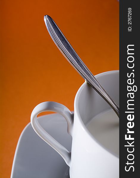 Close up of a cup a dish and a spoon, in a orange background, studio image. Close up of a cup a dish and a spoon, in a orange background, studio image