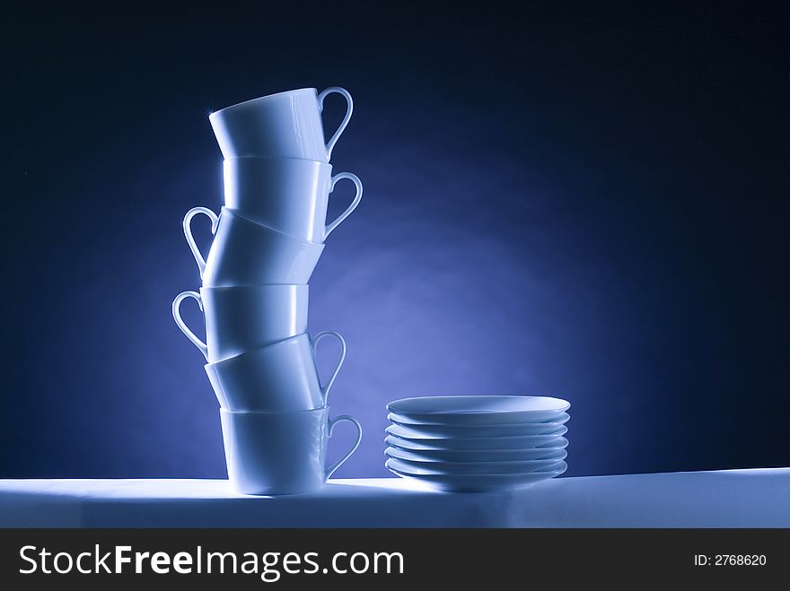 A pile of cups in a s shape whit some dishes in a black and blue background, studio image composition. A pile of cups in a s shape whit some dishes in a black and blue background, studio image composition