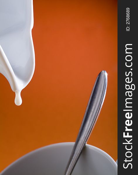 Close up of a drop of milk coming from a jar to a cup in a orange background