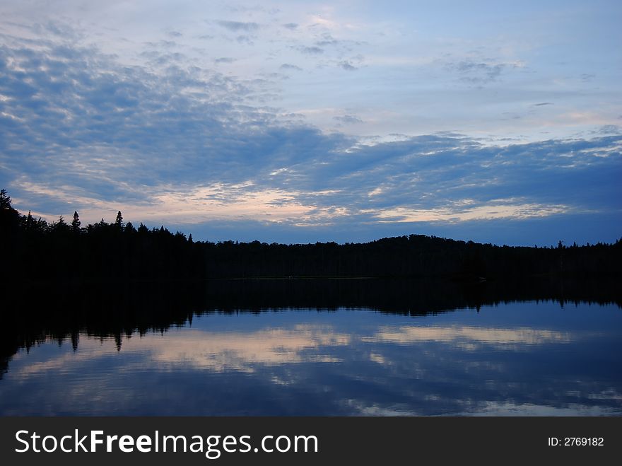 Cloud and sky reflected in lake with silhouetted shoreline. Cloud and sky reflected in lake with silhouetted shoreline