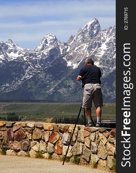 A photographer standing on a wall high above a valley to get his shot. Mountains in the background. A photographer standing on a wall high above a valley to get his shot. Mountains in the background.