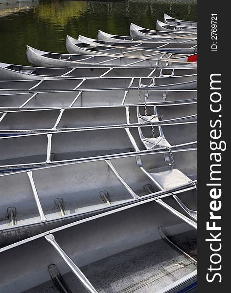 Fourteen empty aluminum camping canoes docked together.