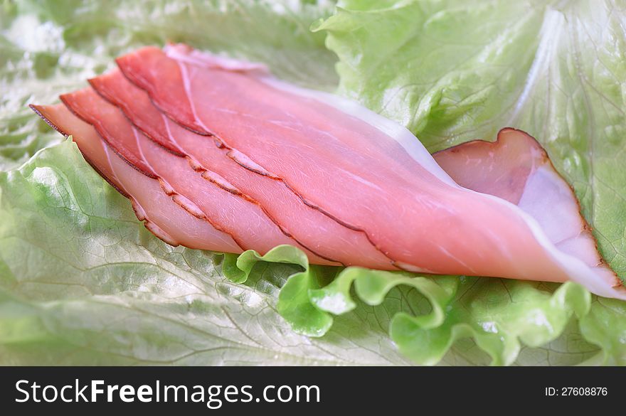 Slices of smoked pork hams are on the leaves of fresh green lettuce. Slices of smoked pork hams are on the leaves of fresh green lettuce