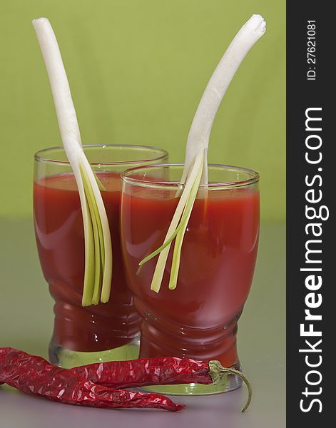 Two glasses of tomato juice with leaves of green onions on a green background