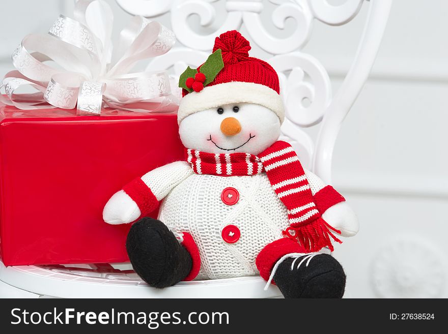 Smiling decorative snowman with red present box sitting on a white vintage chair