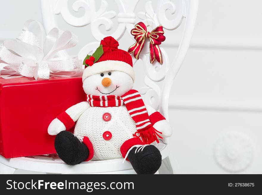 Toy snowman with red box Christmas gift sitting on a white vintage chair